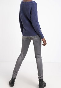 Pull en tricot bleu marine avec une coupe ample et une texture côtelée, associé à un jean gris ajusté et des bottines noires, vu de dos.