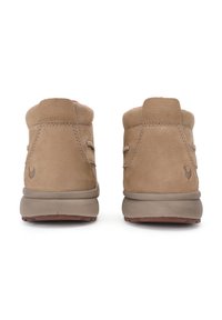 Botas de tobillo de ante marrón con una textura suave, parte superior redondeada y suela de goma. Presentan ventilaciones laterales y un pequeño logo en el talón.