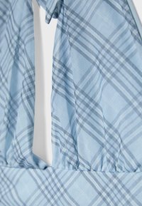 Tissu bleu clair avec un motif à carreaux bleu foncé comportant une couture froncée et un col en forme de goutte d’eau.