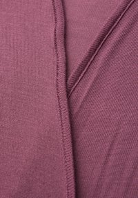 Primer plano de tela morada suave con textura de tejido visible y detalles de costuras superpuestas.