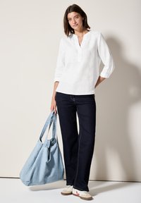 Vit linnetopp med halvpolo, mörk denim vidbyxor och en stor ljusblå toteväska. Vita sneakers med röda accenter.