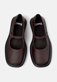Zapatos Mary Jane de cuero marrón con puntera redondeada, suela de goma plana y una correa con hebilla en el empeine. Forro interior texturizado.