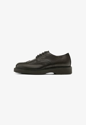 Chaussures brogue en cuir noir avec perforations décoratives, bout rond, six œillets et une semelle en caoutchouc épaisse et texture.