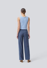 Světle modrý háčkovaný crop top spárovaný s volnými, tmavě modrými kalhotami s jemnou strukturou a elastickým pasem.
