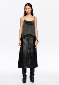 Top de punto gris con adornos florales, superpuesto a una larga falda de cuero negra, combinado con elegantes botas negras. Incluye accesorios sencillos.