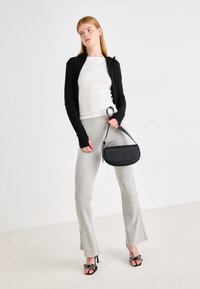 Schwarze langärmlige Zip-Up-Strickjacke, weißes eng anliegendes Oberteil, graue Schlaghose, schwarze Schultertasche und schwarze Sandalen mit Absatz und dekorativen Akzenten.