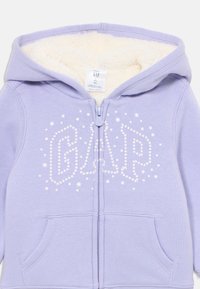 Felpa con zip color lavanda, foderata in pelliccia sintetica, con la scritta "GAP" in strass bianchi e dettagli bianchi a forma di stella; dotata di tasche frontali.
