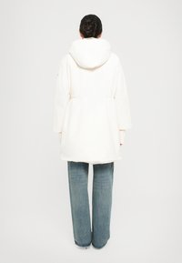 Witte parka met een grote capuchon, een smal taille en brede mouwen. Gecombineerd met lichtblauwe wijde jeans voor een casual look.