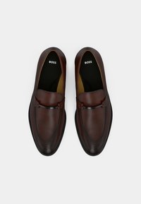 Pruunid nahast loafers, millel on stiilne disain, ümar varvas ja diskreetne brändimine sisetallal. Sile tekstuur, millel on minimaalne detailide hulk.