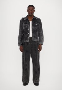 Jachetă din denim negru cu un finisaj texturat, pantaloni largi gri cu accente de cusătură și botine negre. Design minimalist cu un aspect casual.