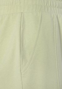Light green sweatpants with textured fabric, elastic waistband, and side pockets. Seam details visible along the fabric surface.