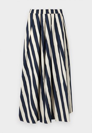 Femme portant une chemise blanche à boutons sur un débardeur bleu marine, un pantalon large à rayures verticales bleu marine et blanc, et des sandales marron.