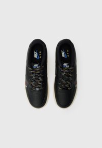 Une paire de baskets Nike Air Force 1 noires avec des lacets multicolores, un logo Nike bleu et jaune à l'intérieur, et des semelles blanches sur un fond blanc.