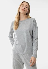 Grijze longsleeve top van zachte, gestructureerde stof. Beschikt over een ronde halslijn en een ontspannen pasvorm, gecombineerd met bijpassende grijze broeken.