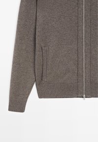 Graue Strickjacke mit Reißverschluss vorne, geripptem Saum und Bündchen sowie Seitentaschen. Der Stoff wirkt weich und warm.