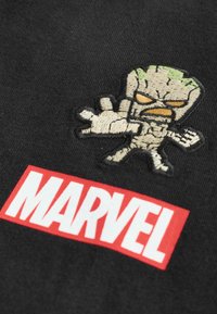 Embroidered Groot character with green top and beige body above red and white Marvel logo on black fabric.