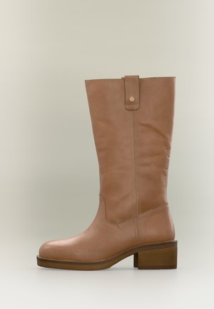 Botte en cuir fauve mi-mollet avec talon bloc, languette de traction et coutures visibles le long de la tige et du pied.