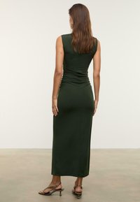 Robe maxi sans manches, verte foncée, avec fronces au dos. Tissu lisse et extensible avec une silhouette ajustée et un ourlet long.