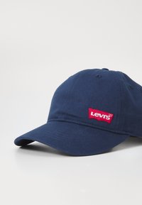 Námořnická modrá bavlněná kšiltovka s zakřiveným kšiltem a červeným vyšitým logem Levi's na přední straně. Má šest ventilačních otvorů.