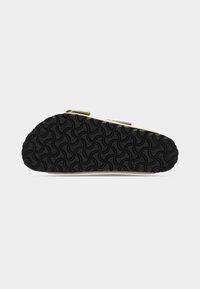 Υποδήματα με μαύρη καουτσούκ σόλα που έχει κυματιστό μοτίβο, μπεζ επάνω μέρος με δύο ρυθμιζόμενους ιμάντες και υφή τελειώματος.