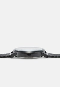 Ceas de metal negru cu carcasă rotundă, curea texturată neagră și față din sticlă clară. Prezintă o coroana rotundă simplă pe lateral.