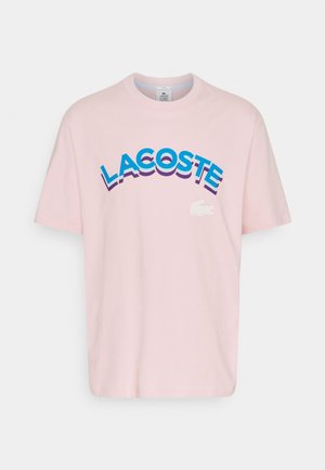 Roze katoen T-shirt met vetgedrukte, gestileerde "LACOSTE" tekst in blauw en paars, met een wit krokodillenlogo aan de voorkant.