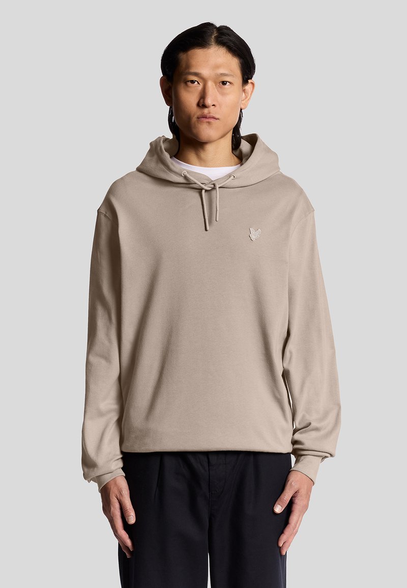 Felpa in cotone beige con tasca a marsupio frontale, cordini sul cappuccio e un piccolo logo sul petto. Vestibilità ampia e maniche lunghe.