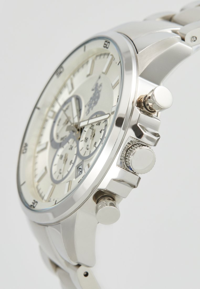 Montre-bracelet en métal argenté avec un cadran rond, trois sous-cadrans et une couronne texturée. Présente un cadran de couleur claire et des index horaires bien visibles.