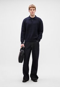 Polo de malha azul-marinho, calças de denim escuras e largas, e mala estruturada preta. Textura suave, punhos canelados e detalhes de design minimalistas.