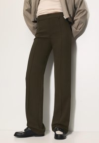 Bredde ben olivengrønne bukser lavet af glat stof, med for-pleats og en skræddersyet pasform. Kombineret med sorte slip-on sko.