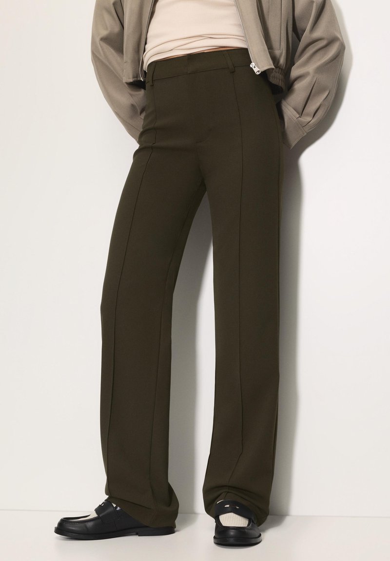 Bredde ben olivengrønne bukser lavet af glat stof, med for-pleats og en skræddersyet pasform. Kombineret med sorte slip-on sko.