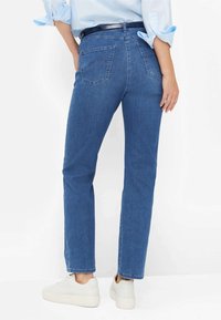 Jean en denim bleu avec une jambe droite, deux poches arrière et un ourlet propre. Associé à des baskets blanches pour un look décontracté.