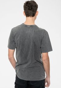 Gray cotton t-shirt with a crew neck, short sleeves, and a worn look. Displays subtle texture and stitching detail at the collar.