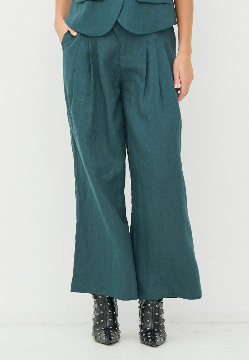 Teal linen wide-leg pants with front pleats, featuring side pockets. Paired with black studded ankle boots for contrast.