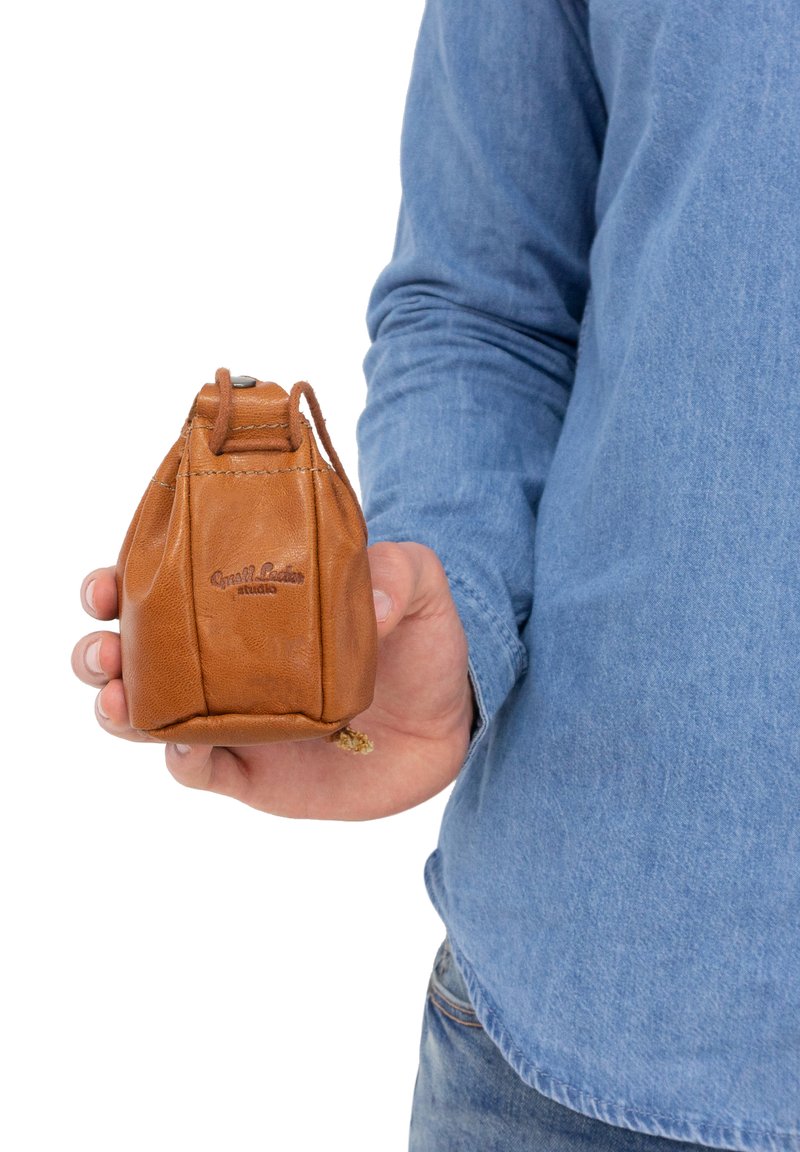 Braune Leder-Zugtasche mit abgerundetem Boden, strukturiertem Oberflächen und geprägt Logo. Handtragend, zeigt die kleine Größe und das schlichte Design.