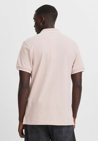 Polo shirt i lyserød med korte ærmer, ribbet krave og et struktureret stof. Med en sideslæb ved sømmen og kontrasterende kant.