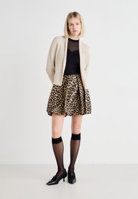 Beige strikket cardigan over en svart, gjennomsiktig topp og et leopardmønstret skjørt. Svart knesokker og spisse, svarte sko fullfører antrekket.