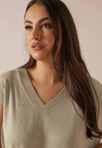 Stickad beige tröja med V-ringning, korta ärmar och ribbade detaljer. Tyget har en mjuk textur och en lätt glans.