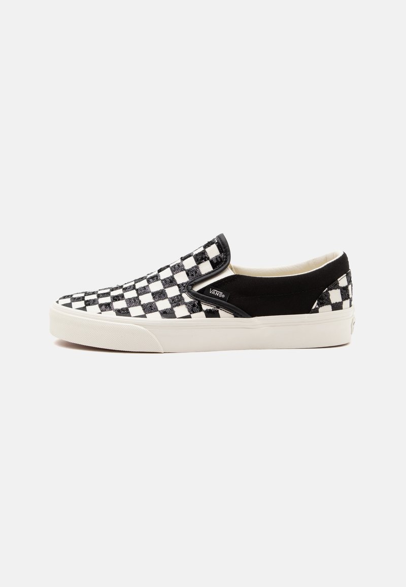 Baskets Vans slip-on à carreaux noirs et blancs avec semelle blanche et panneaux latéraux élastiques noirs, photographiées de profil sur fond blanc.