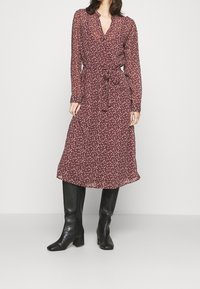 Burgundy blommig omslagsklänning med långa genomskinliga ärmar, knytmidja och knappdetaljer; matchad med knähöga svarta klackstövlar.