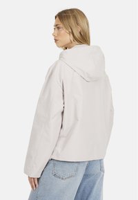 Veste à capuche gris clair avec une coupe décontractée, texture lisse et manches longues. Comprend un empiècement au dos et une longueur courte.