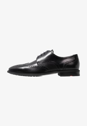 Chaussure habillée en cuir noir avec des détails de brogue, un bout arrondi, six œillets et une finition lisse avec une subtile texture sur les côtés.