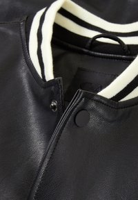 Veste en cuir noir avec un col côtelé rayé blanc et noir, fermeture par boutons-pression et détail de surface texturée.