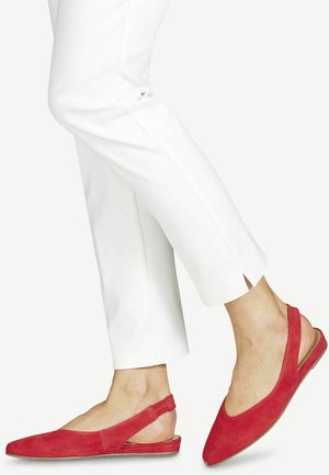 Bailarinas de ante rojo con punta afilada y tacón minimalista. Presentan un diseño con corte y una simple correa en el tobillo. Se llevan con pantalones blancos.