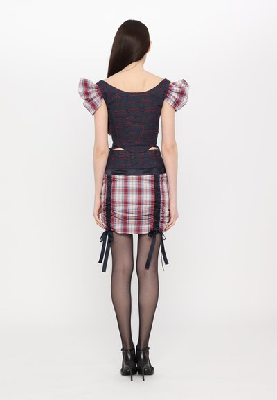 Two-piece outfit featuring a fitted navy top with red patterns and a plaid mini skirt, accented with side ruching and ribbon ties.