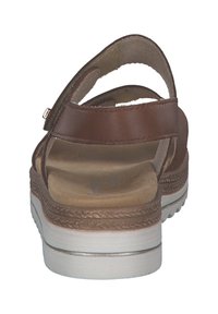 Brown leather sandal with an open back, adjustable strap, and light-colored sole. Features a textured footbed and stitched detailing.