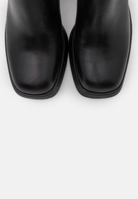 Mustat nahka nilkkasaappaat, joissa on nelikulmainen varvas, sileä pinta ja minimalistinen muotoilu. Ei näkyviä kiinnikkeitä tai kuvioita.