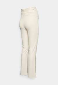 Calças cor creme em canalé com uma cintura ajustada, alargadas na parte inferior. Apresentam um tecido suave e texturizado e um design sem costuras.