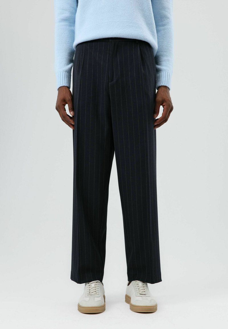 Marineblauwe pantalon met krijtstreep in een relaxed fit, voorzien van een geplooide voorkant, gemaakt van een textuurstof, gecombineerd met witte sneakers.