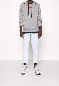 Sudadera gris con una etiqueta de logo roja, combinada con jeans recortados de un azul claro y zapatillas grises. Textura suave y corte relajado.